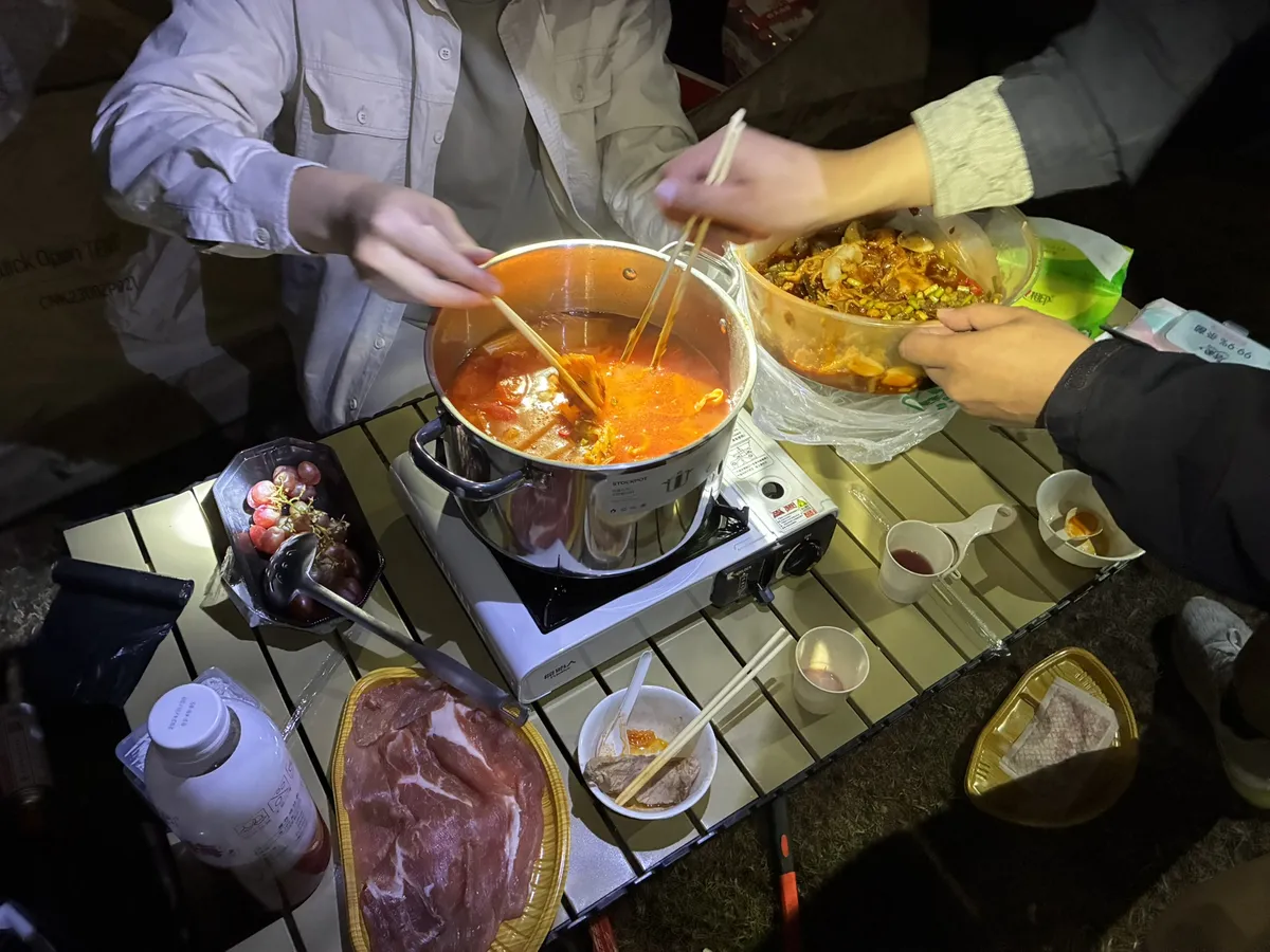 夜里的折叠桌上,卡式炉架着汤锅煮火锅,旁边摆着肉片、配菜和纸杯,只有手入镜